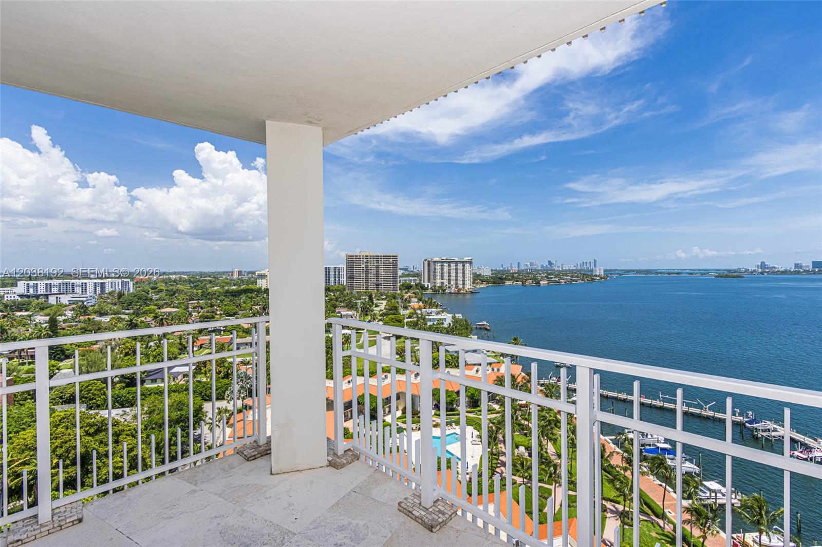 A balcony with a white railing overlooks a bay, residential buildings, and a distant city skyline — 4000 Towerside Ter # 1701, Miami FL 33138, MIAMI, FL