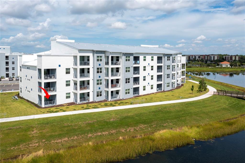An exterior view of a multi-story apartment building with balconies overlooking a pond and walkway — 3161 PARADOX CIRCLE UNIT # 108, KISSIMMEE, FL