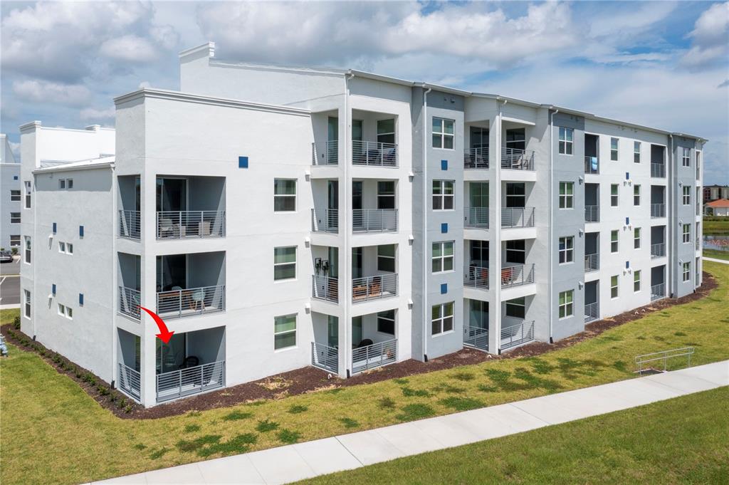 An exterior view of a multi-story apartment building with a red arrow pointing to a balcony — 3161 PARADOX CIRCLE UNIT # 108, KISSIMMEE, FL
