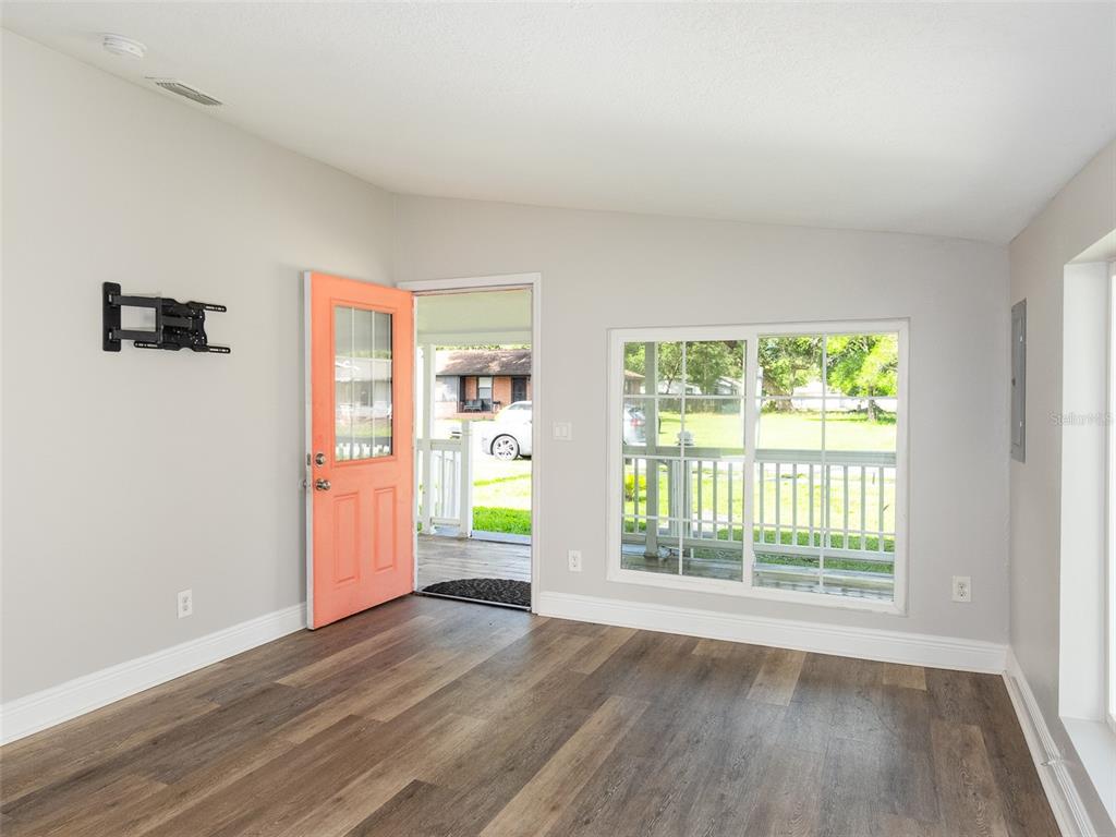 A living room with wood-look flooring, a coral front door, and a large sliding window — 1105 WILLOW AVENUE, SANFORD, FL