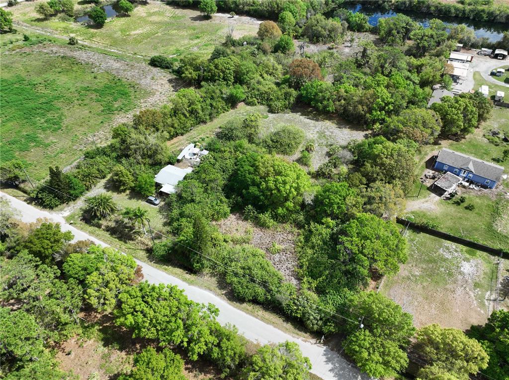 An aerial view shows a wooded lot with a small house and a paved road — 1518 27TH STREET SE, RUSKIN, FL