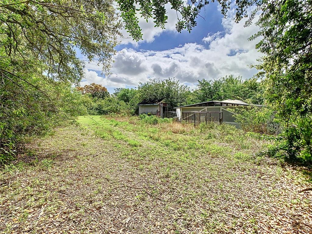 A grassy yard leads toward a small shed and a screened-in structure under trees — 1518 27TH STREET SE, RUSKIN, FL
