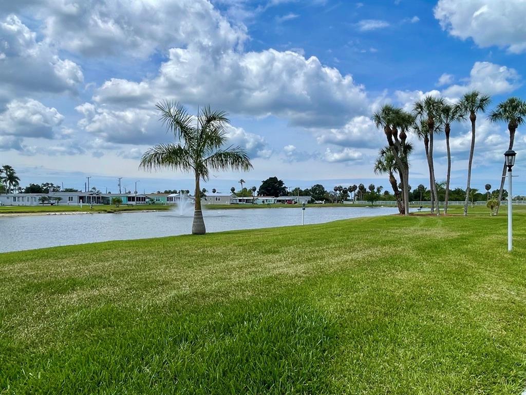 A grassy lawn overlooks a pond with a fountain and palm trees under a cloudy sky — 152 SHADY LANE UNIT 152, PALMETTO, FL