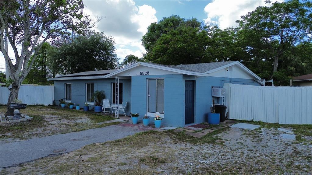 A blue, single-story concrete block house with a gravel driveway and white privacy fencing — 5828 HARCOURT AVENUE, ORLANDO, FL