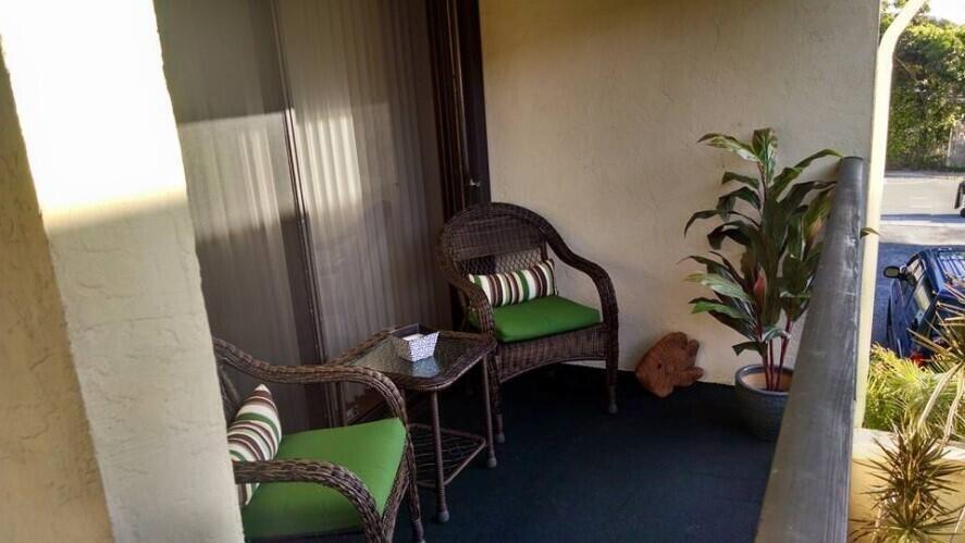A small balcony features two wicker chairs, a glass-topped side table, and a potted plant — 120 N M Street # L, FL 33460, FL