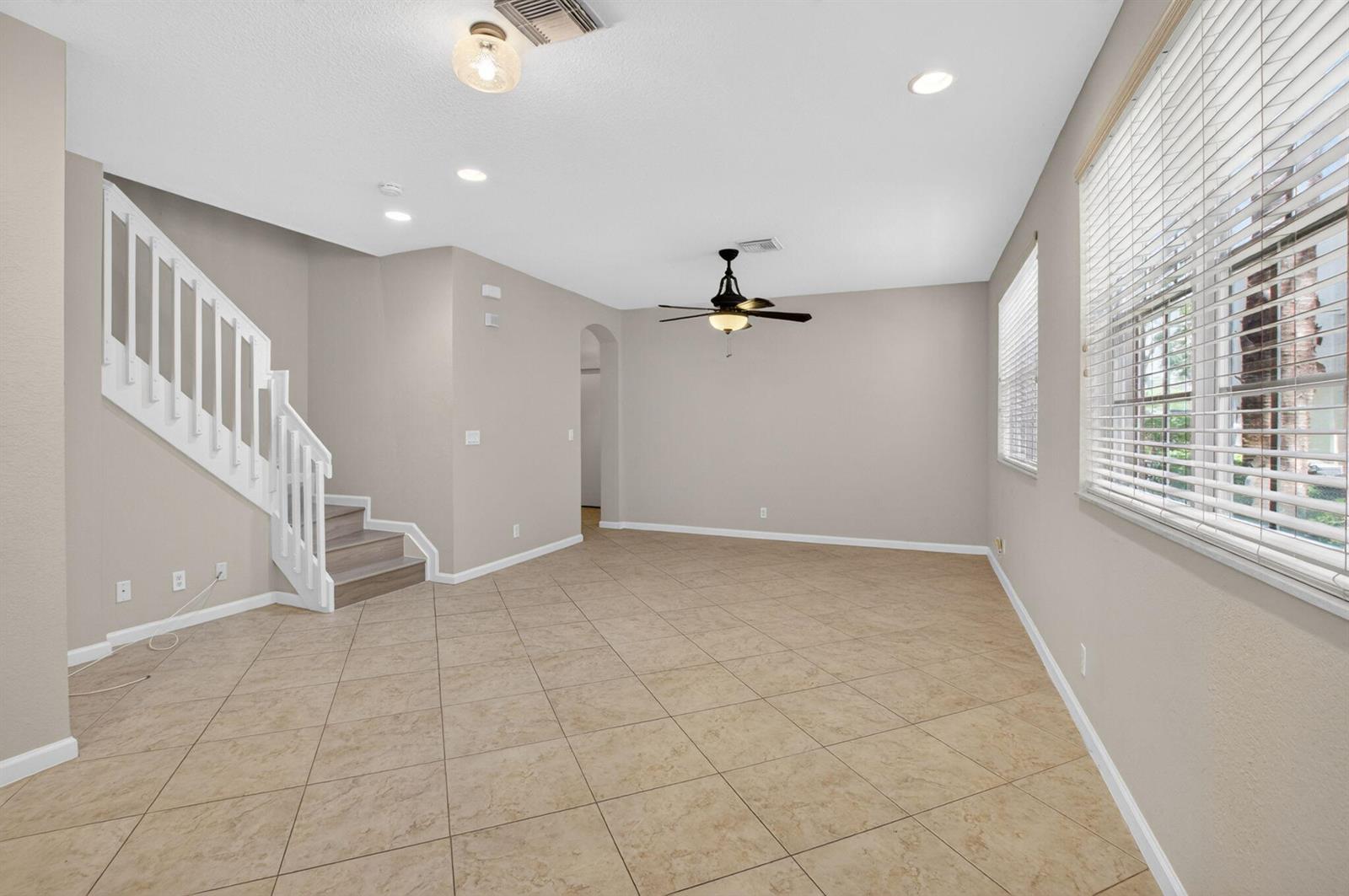 An empty living room features beige walls, tile flooring, a ceiling fan, and a staircase — 1418 W Wickham Circle # B, Delray Beach FL 33445, DELRAY BEACH, FL