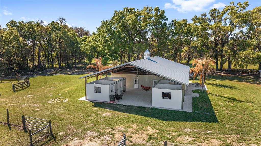 An aerial view shows a metal-roofed barn with open-air horse stalls on a grassy lot — 13869 S HWY 475, SUMMERFIELD, FL