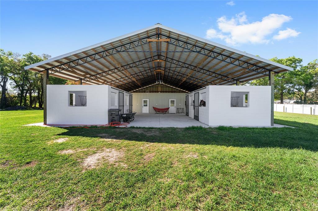 An open-air metal barn structure features two rows of white stalls under a large roof — 13869 S HWY 475, SUMMERFIELD, FL