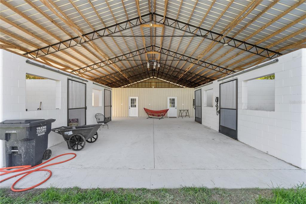 A covered barn aisle features concrete flooring, white block walls, and several horse stall doors — 13869 S HWY 475, SUMMERFIELD, FL