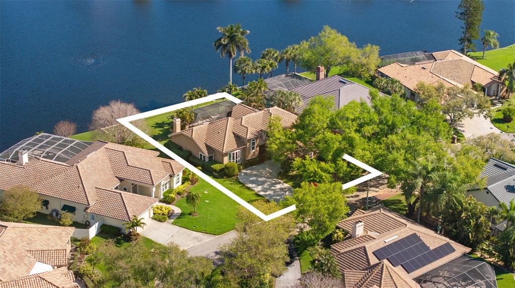 An aerial view shows a tan house with a tiled roof and pool enclosure by water — 4731 COCONUT PALM CIRCLE NE, ST PETERSBURG, FL
