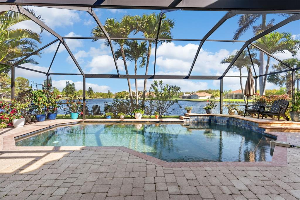 A screened-in pool patio features brick pavers, potted plants, and a view of a lake — 4731 COCONUT PALM CIRCLE NE, ST PETERSBURG, FL