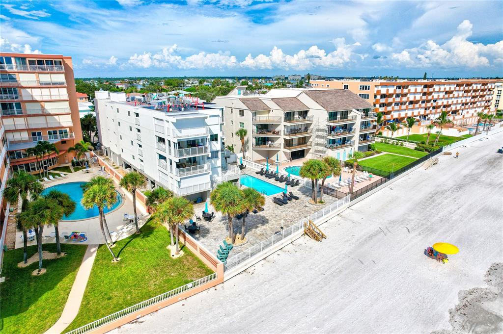 An elevated view shows a swimming pool, patio furniture, palm trees, and a sandy beach — 16332 GULF BOULEVARD UNIT 1C, REDINGTON BEACH, FL