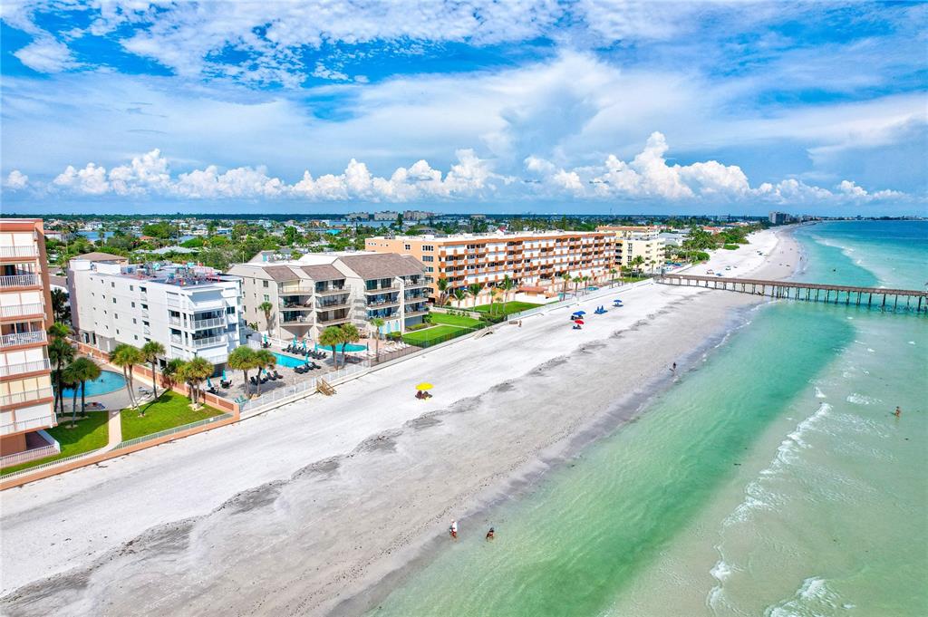 An aerial view shows beachfront condominiums, a sandy beach, and a pier extending into the ocean — 16332 GULF BOULEVARD UNIT 1C, REDINGTON BEACH, FL