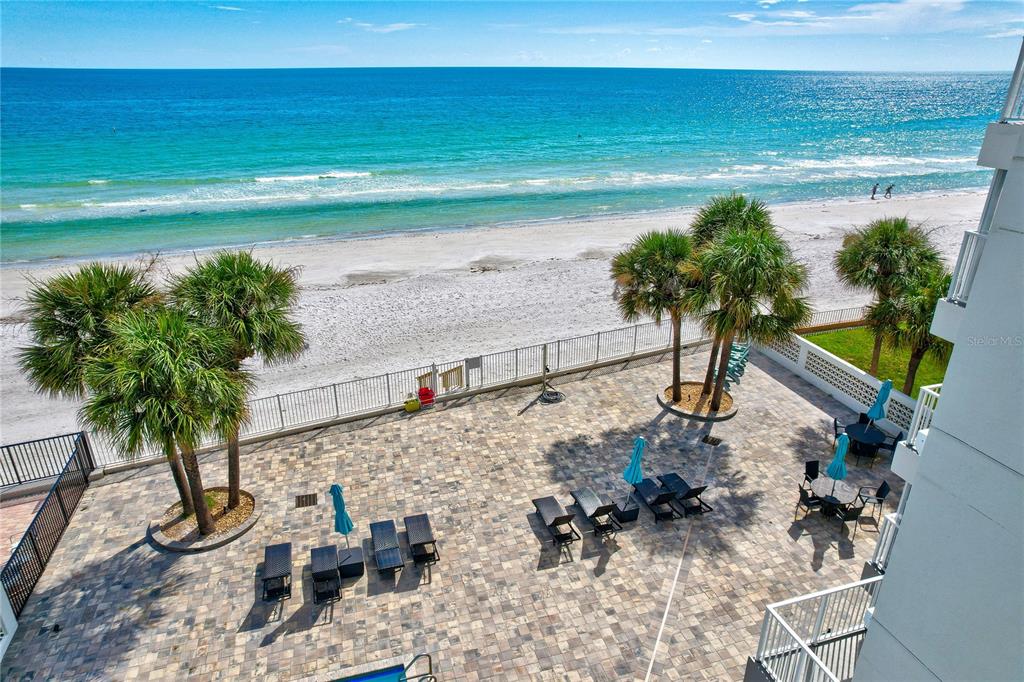An elevated view of a paved patio with lounge chairs overlooking a sandy beach — 16332 GULF BOULEVARD UNIT 1C, REDINGTON BEACH, FL