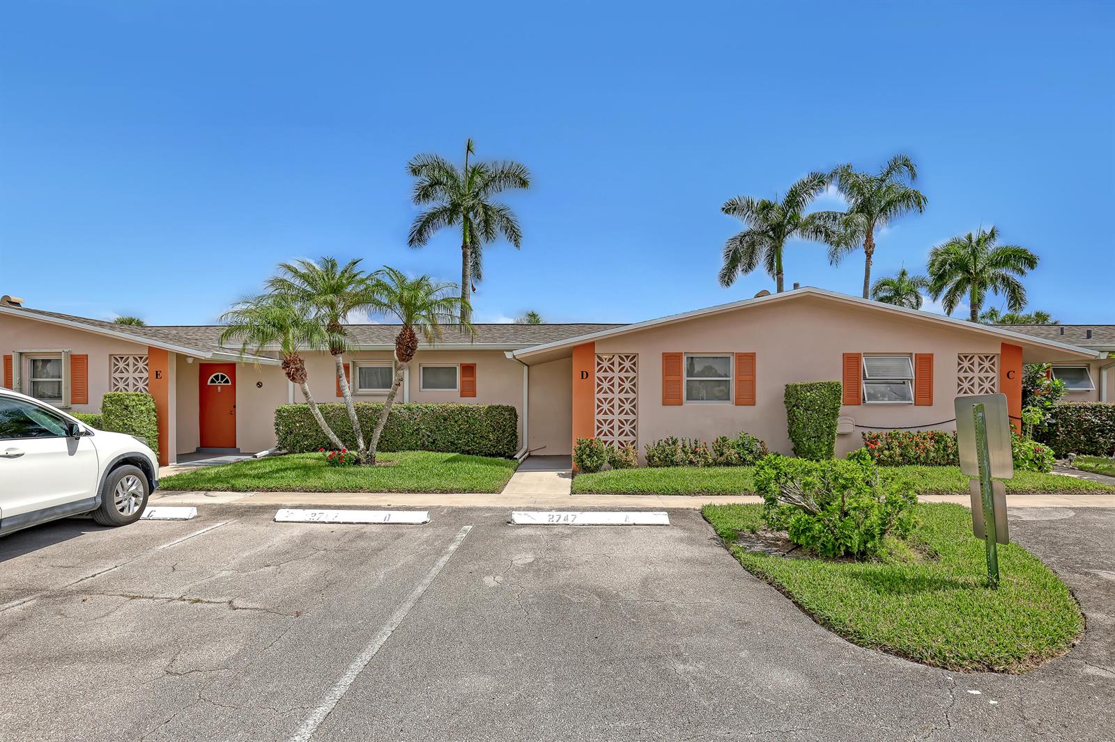 A single-story apartment building with a parking lot, palm trees, and labeled unit entrances — 2747 Dudley Drive E # D, West Palm Beach FL 33415, WEST PALM BEACH, FL