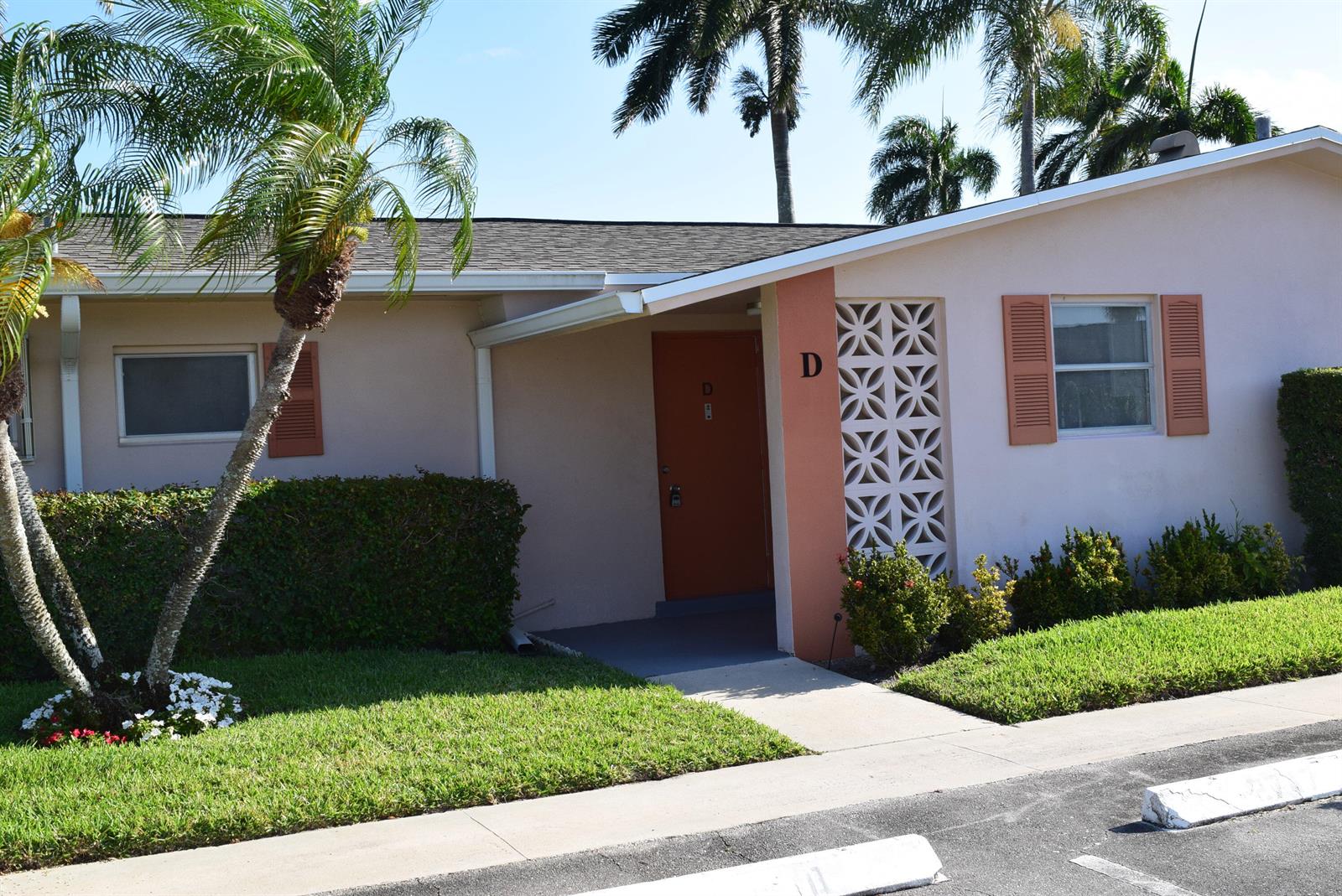 A single-story building exterior features a peach-colored facade, a brown door marked D, and landscaping — 2747 Dudley Drive E # D, West Palm Beach FL 33415, WEST PALM BEACH, FL