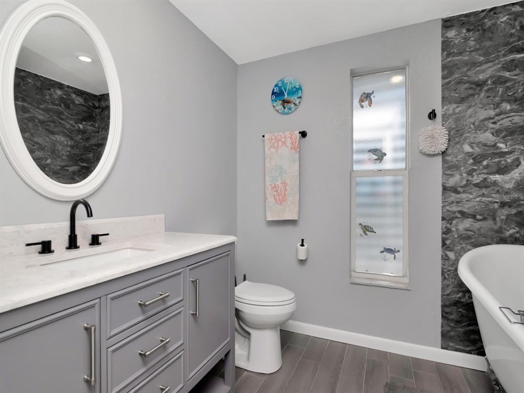 A bathroom features a grey vanity, white countertop, oval mirror, toilet, and a freestanding tub — 13615 STACEY DRIVE, HUDSON, FL
