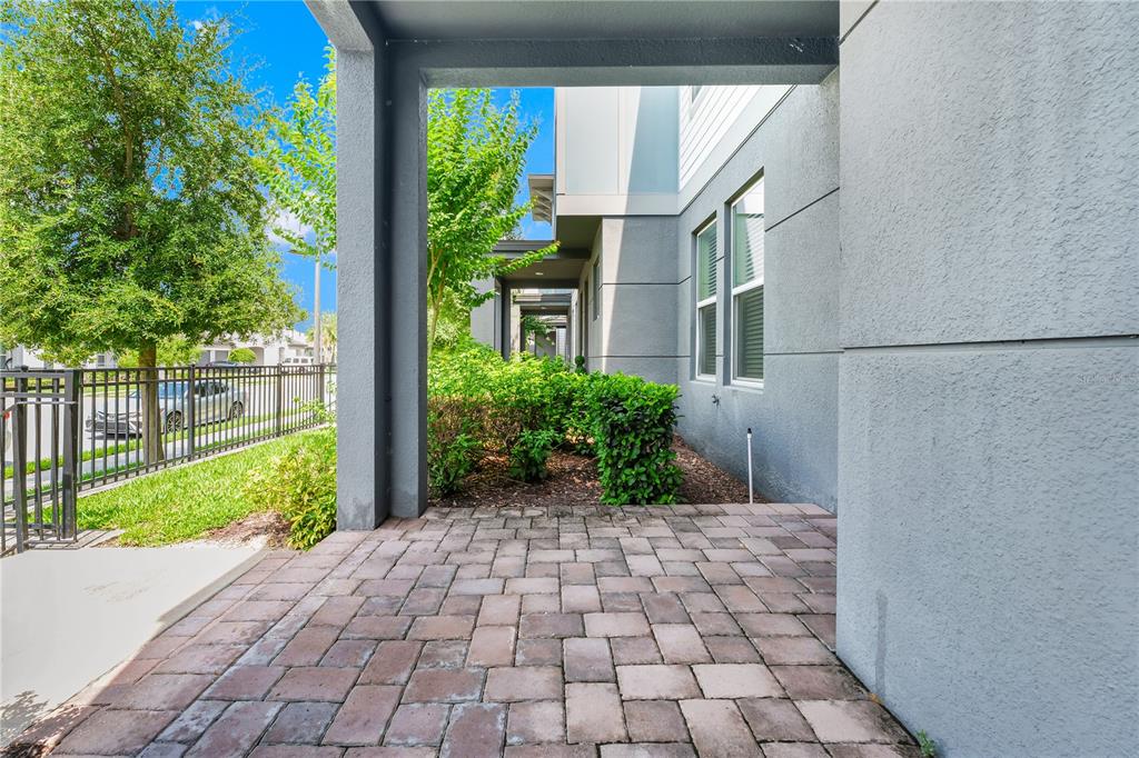 A paved patio sits beneath a covered entryway next to a gray building and landscaping — 7381 ALPINE BUTTERFLY LANE, ORLANDO, FL