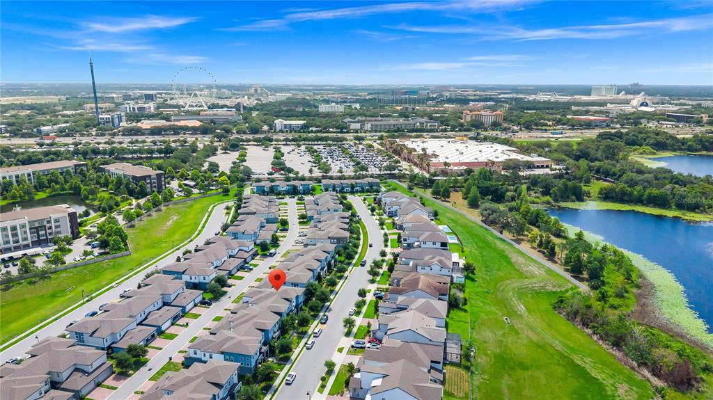 An aerial view shows a residential neighborhood of townhomes near a lake and city skyline — 7381 ALPINE BUTTERFLY LANE, ORLANDO, FL