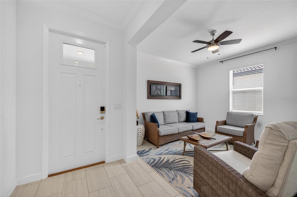 A living room features a white front door, wicker furniture, a ceiling fan, and tile flooring — 5513 LITTLE PATH DRIVE, WIMAUMA, FL