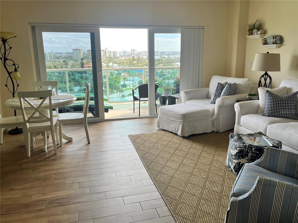 A living and dining area with tile floors, white furniture, and a balcony overlooking city buildings — 880 MANDALAY AVENUE UNIT S806, CLEARWATER BEACH, FL