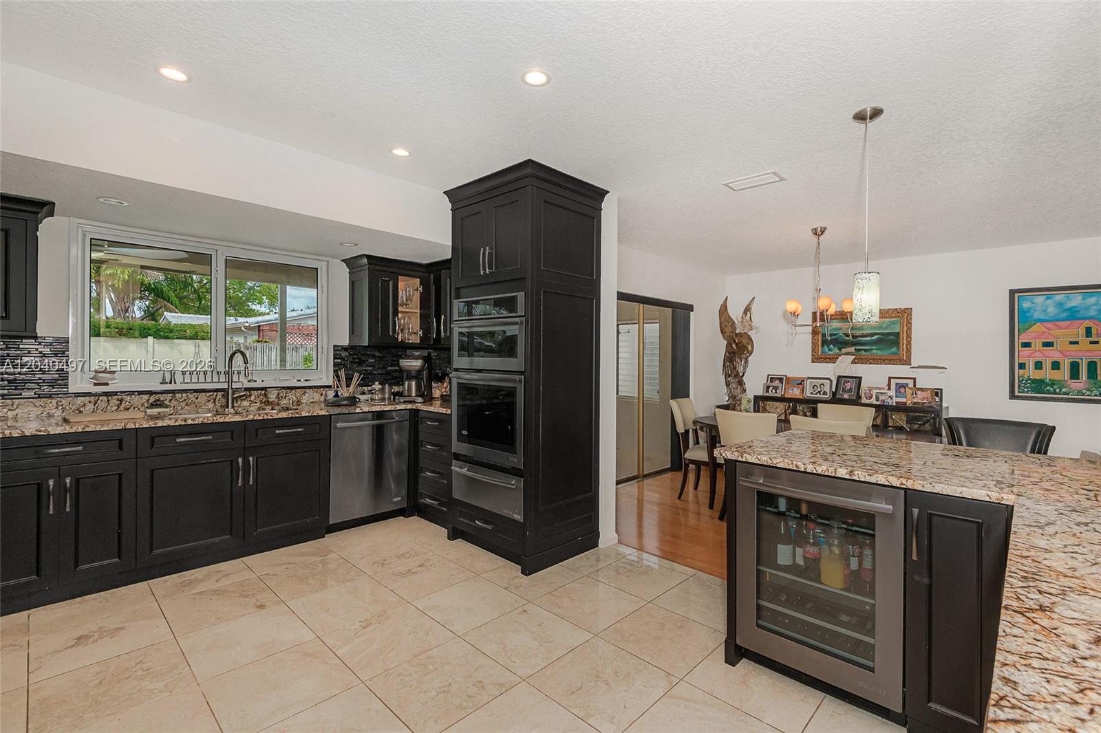 A kitchen features dark cabinetry, granite countertops, stainless steel appliances, and a wine refrigerator — 3900 N 43rd Ave, Hollywood FL 33021, HOLLYWOOD, FL