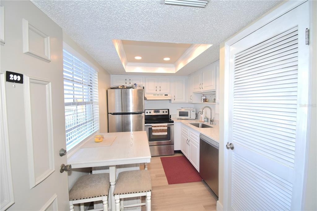 A kitchen features white cabinets, stainless steel appliances, a dining table, and a louvered door — 952 VIRGINIA STREET UNIT 209, DUNEDIN, FL