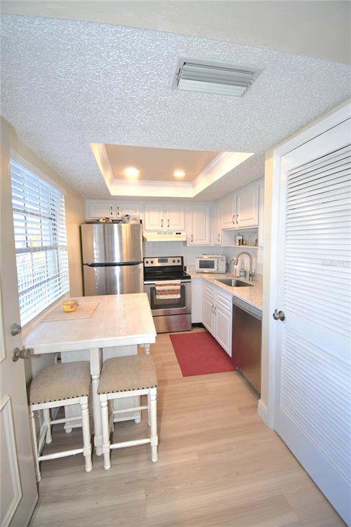 A kitchen features white cabinets, stainless steel appliances, a dining table with stools, and flooring — 952 VIRGINIA STREET UNIT 209, DUNEDIN, FL