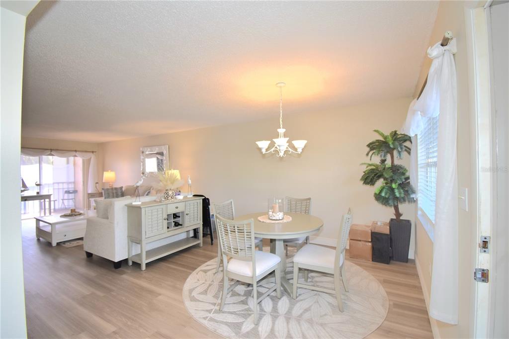 A dining area with a round table and chairs sits adjacent to a living room — 952 VIRGINIA STREET UNIT 209, DUNEDIN, FL