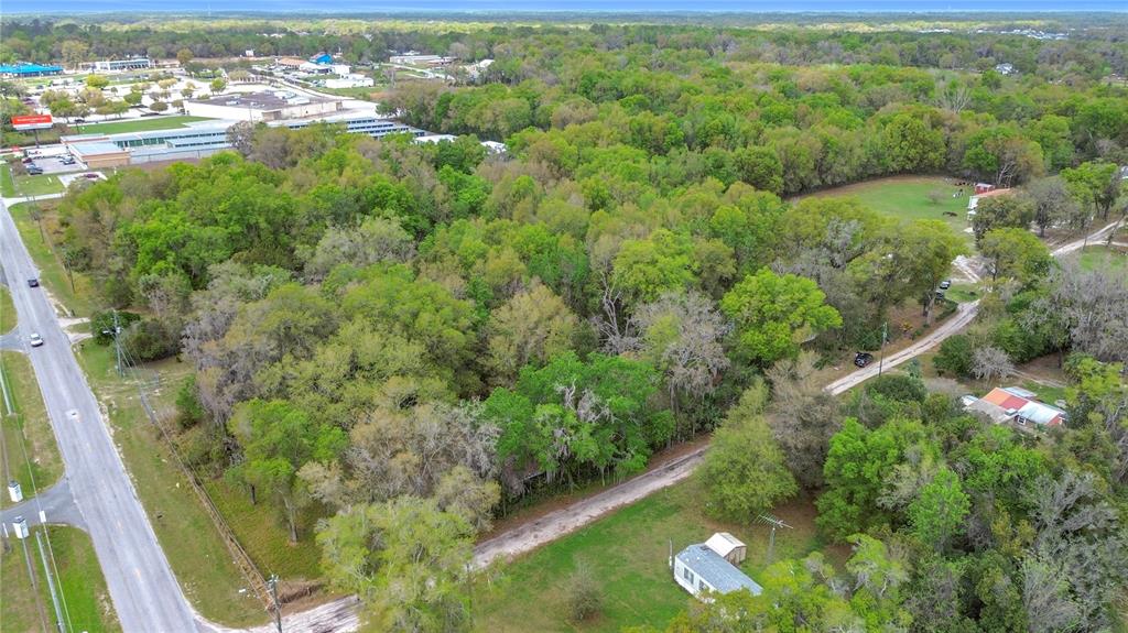 An aerial view shows a wooded lot bordered by a road and nearby commercial buildings — 10160 SE 49TH COURT, BELLEVIEW, FL