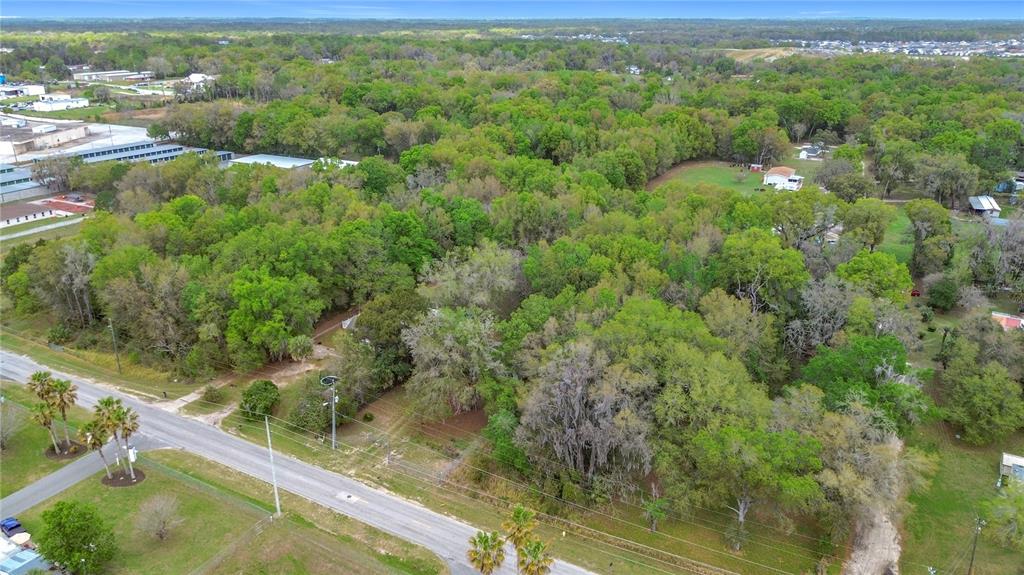 An aerial view shows a wooded lot adjacent to a paved road and nearby buildings — 10160 SE 49TH COURT, BELLEVIEW, FL