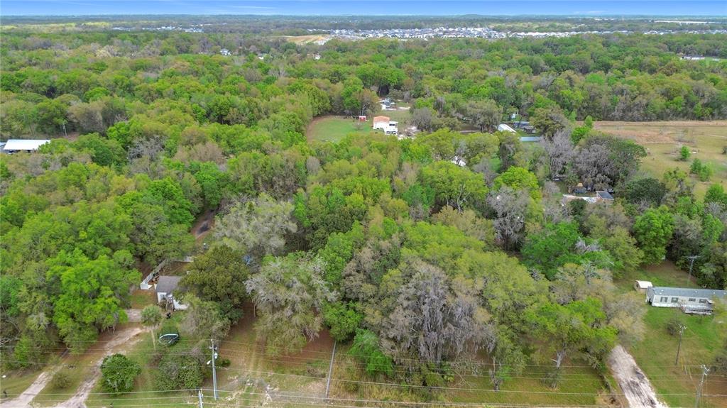 An aerial view shows a wooded residential property with several houses and dirt driveways — 10160 SE 49TH COURT, BELLEVIEW, FL