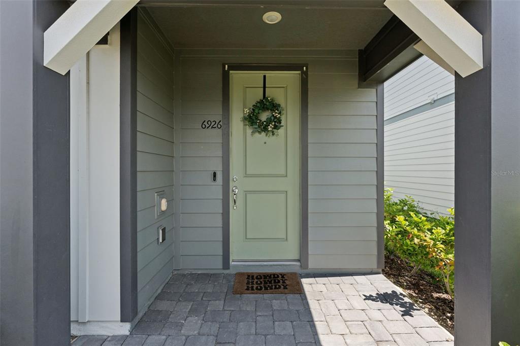 A light green front door with a wreath sits under a covered entryway with pavers — 6926 REVERIE PARK AVENUE, ORLANDO, FL