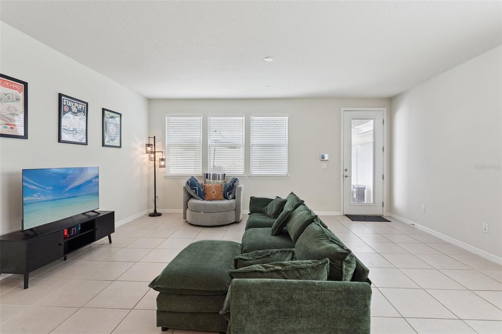 A living room features a green sectional sofa, a television, and a round accent chair — 6926 REVERIE PARK AVENUE, ORLANDO, FL