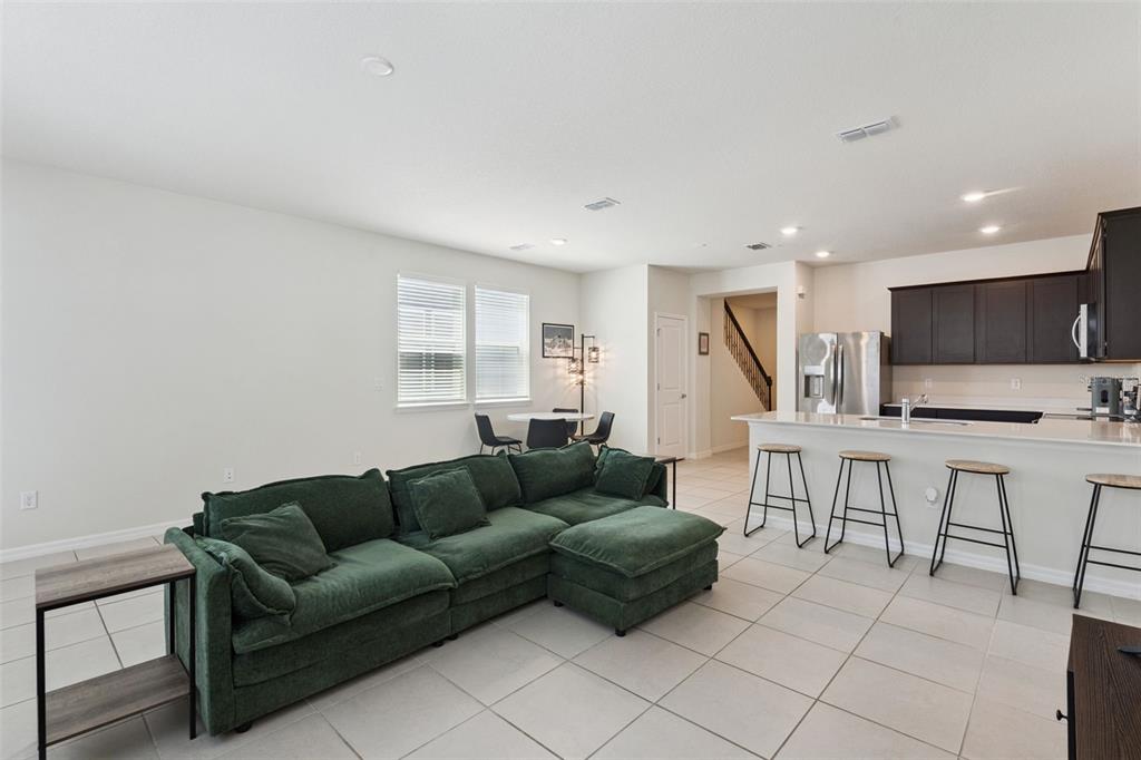 An open-concept living room features a green sectional sofa, tile flooring, and an adjacent kitchen — 6926 REVERIE PARK AVENUE, ORLANDO, FL