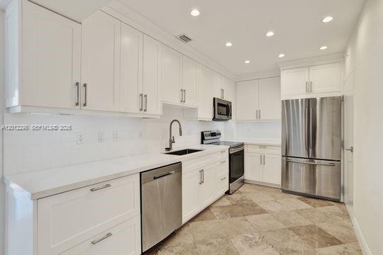 A modern kitchen features white cabinets, stainless steel appliances, and light-colored stone tile flooring — 90 Edgewater # 18, Coral Gables FL 33133, CORAL GABLES, FL