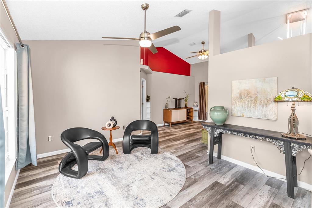 A living room features two black chairs on a round rug, wood-look flooring, and vaulted ceilings — 105 BREEZEWOOD DRIVE, DEBARY, FL