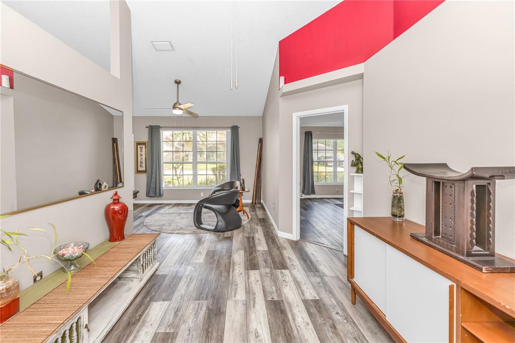 A bright living area with vaulted ceilings, wood-look flooring, and a red accent wall — 105 BREEZEWOOD DRIVE, DEBARY, FL