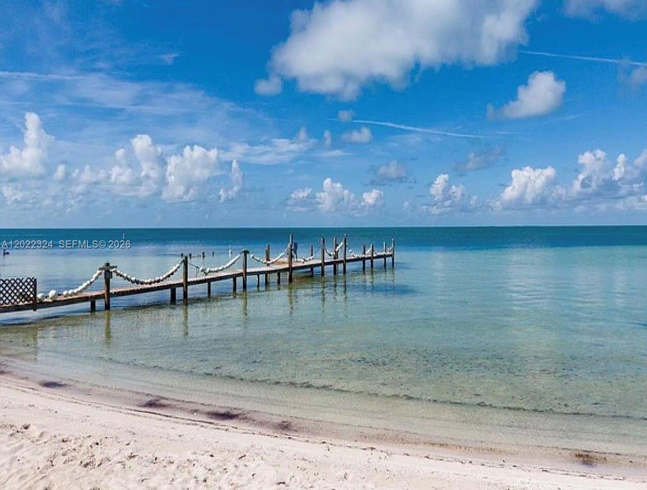 A wooden dock extends into calm, clear ocean water under a blue, cloudy sky — 102 Venetian Dr # 102, Islamorada FL 33036, ISLAMORADA, FL