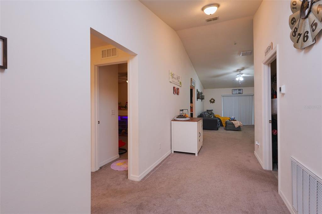 A carpeted hallway leads to a living area with a ceiling fan and sliding doors — 1537 BAYWOOD VILLAGE COURT, MOUNT DORA, FL