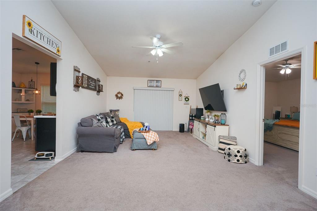 A living room with beige carpet, a grey sectional sofa, and a wall-mounted television — 1537 BAYWOOD VILLAGE COURT, MOUNT DORA, FL