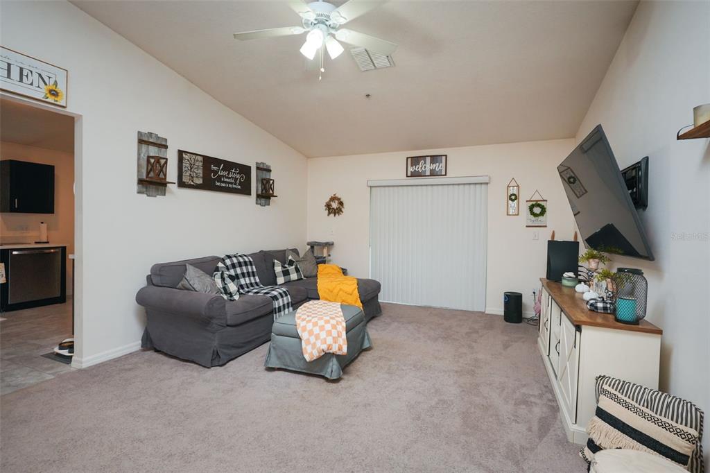 A living room features a grey sectional sofa, a television on a console, and sliding doors — 1537 BAYWOOD VILLAGE COURT, MOUNT DORA, FL