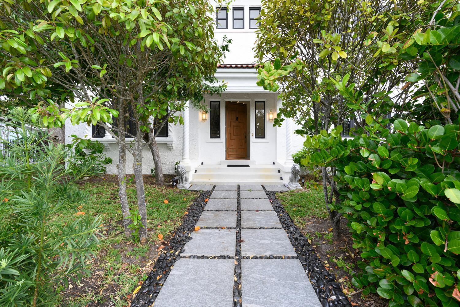A stone walkway leads to the front entrance of a white house with a wooden door — 1629 S Lakeside Drive, FL 33460, FL