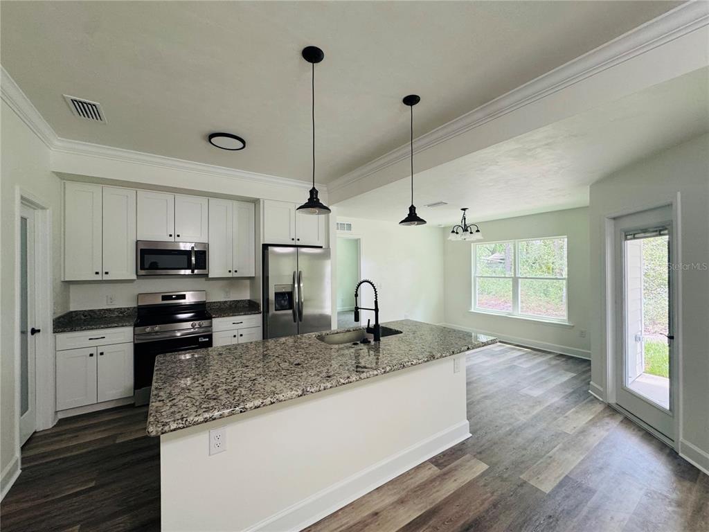 A kitchen features white cabinets, granite countertops, a center island, and wood-look flooring — 10131 NE 80TH STREET, BRONSON, FL
