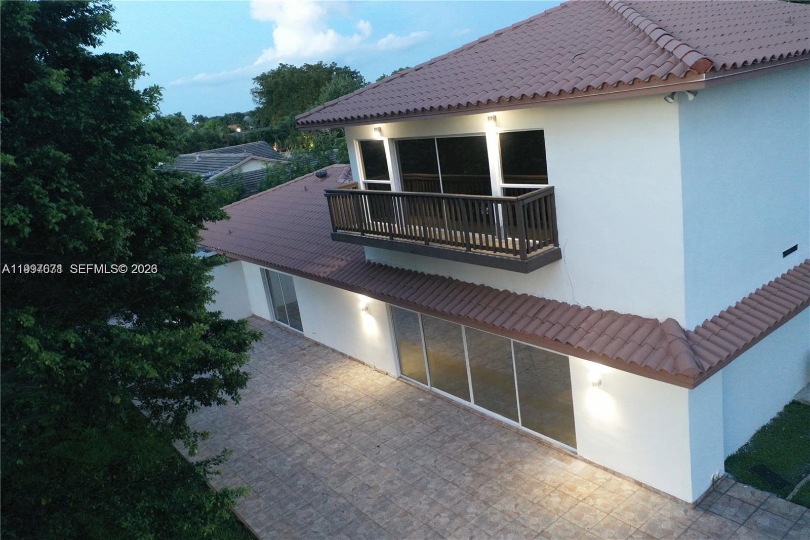 An exterior view of a two-story house with a balcony, tiled roof, and patio — 19740 W Saint Andrews Dr, Hialeah FL 33015, HIALEAH, FL