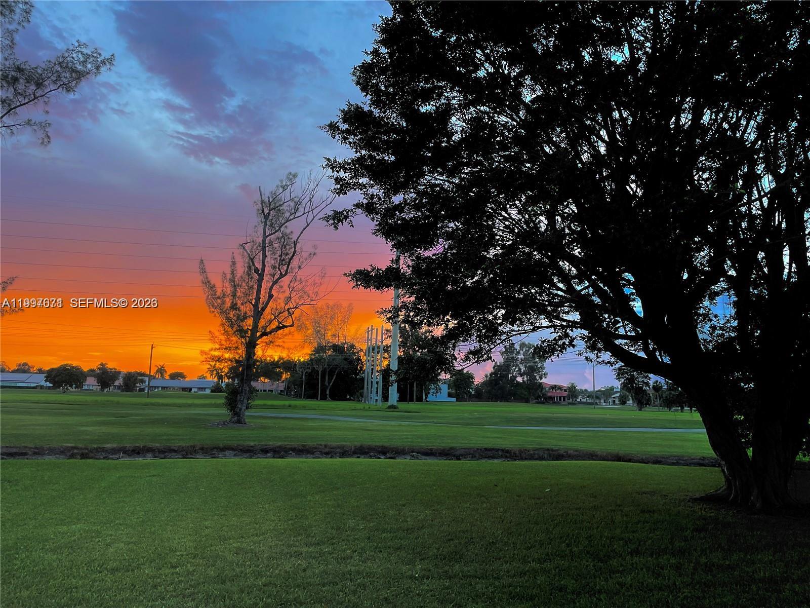 A large tree frames a view of a grassy field during a vibrant sunset — 19740 W Saint Andrews Dr, Hialeah FL 33015, HIALEAH, FL