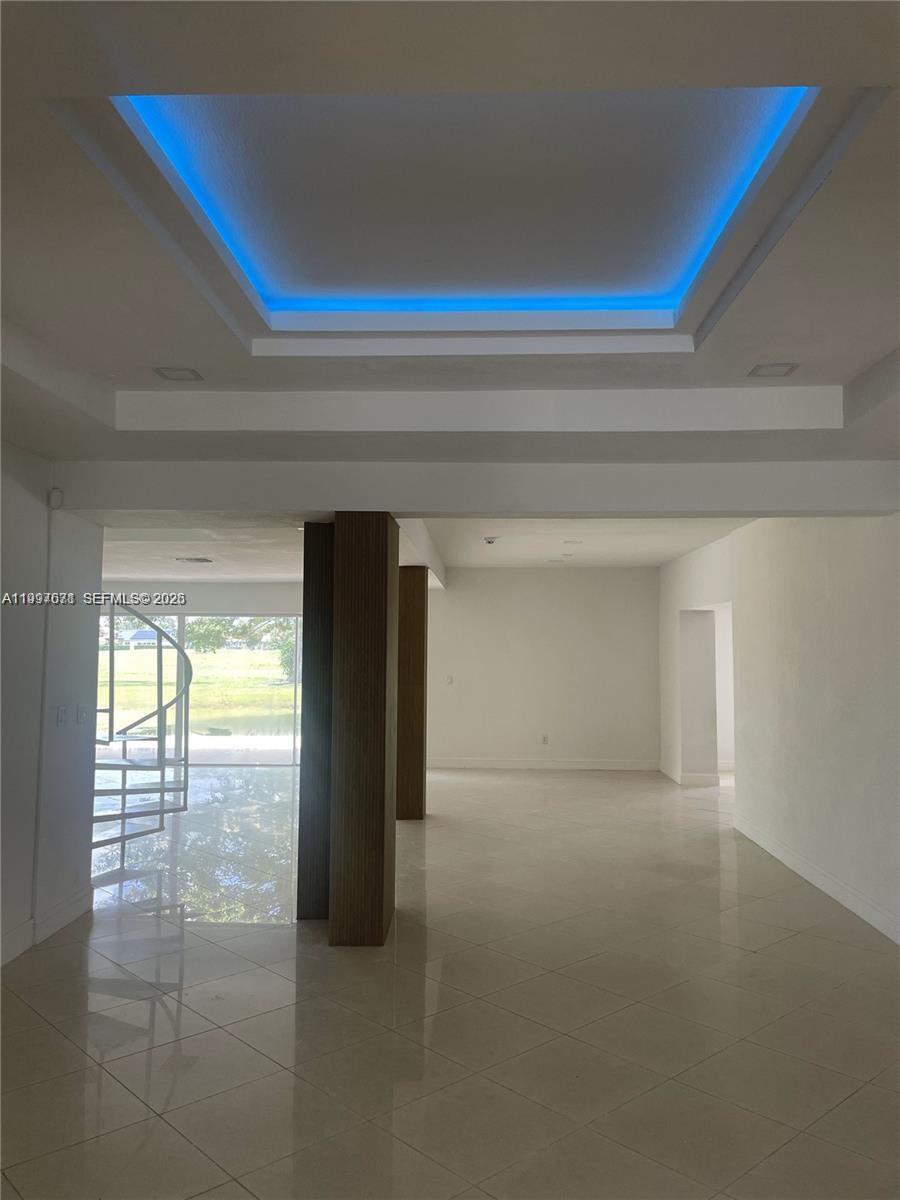 An open living area features a blue-lit tray ceiling, tile flooring, and a spiral staircase — 19740 W Saint Andrews Dr, Hialeah FL 33015, HIALEAH, FL