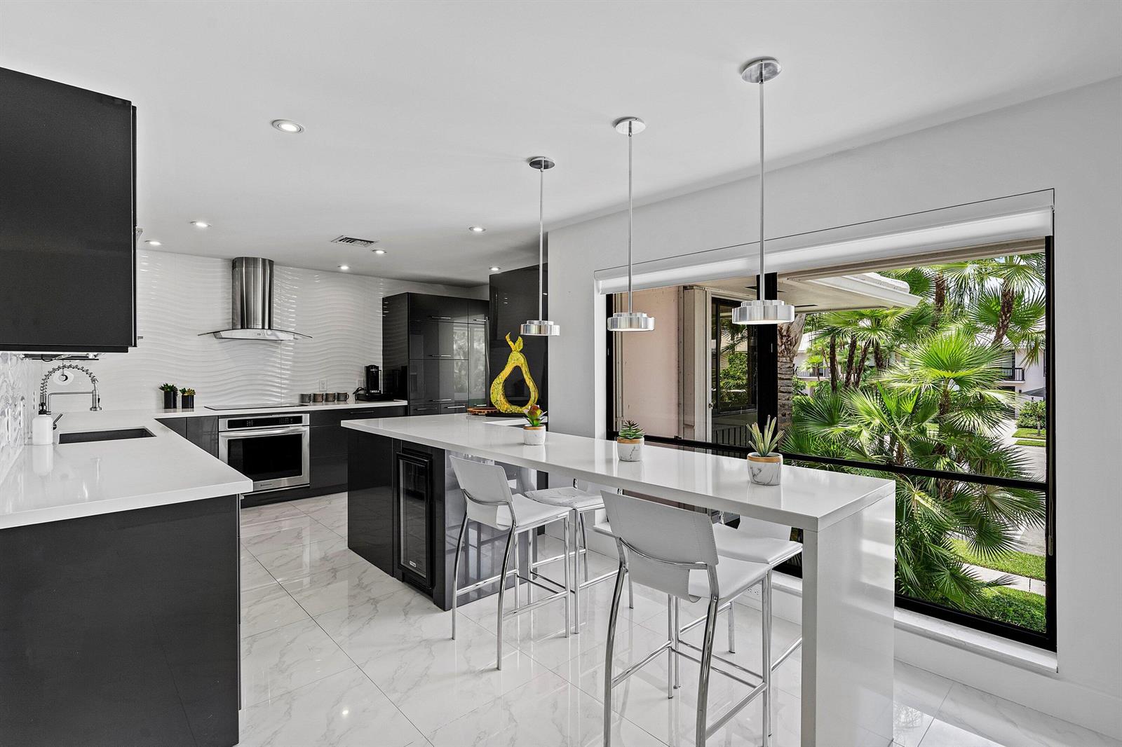 A modern kitchen features dark cabinetry, white countertops, marble-look tile floors, and a breakfast bar — 3808 Quail Ridge Drive N, Boynton Beach FL 33436, BOYNTON BEACH, FL