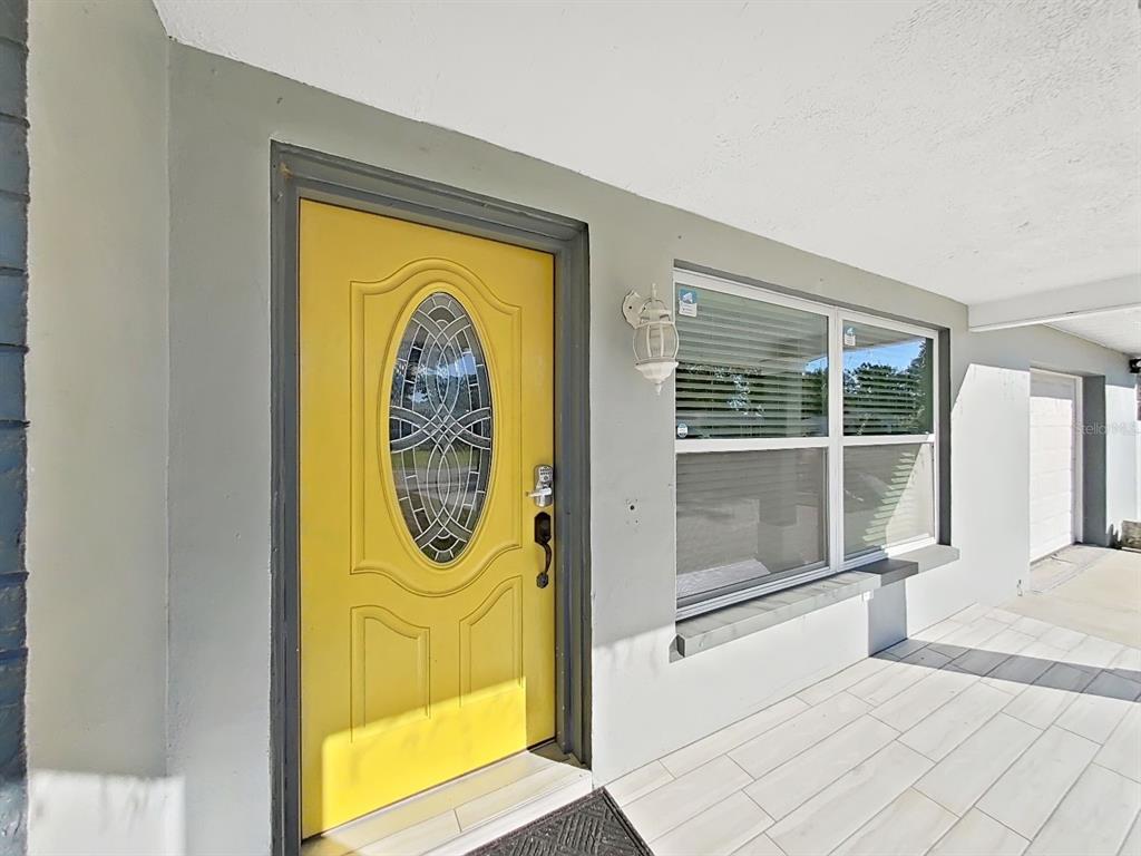 A yellow front door with an oval glass insert sits next to a large window — 1837 AUDREY DRIVE, CLEARWATER, FL
