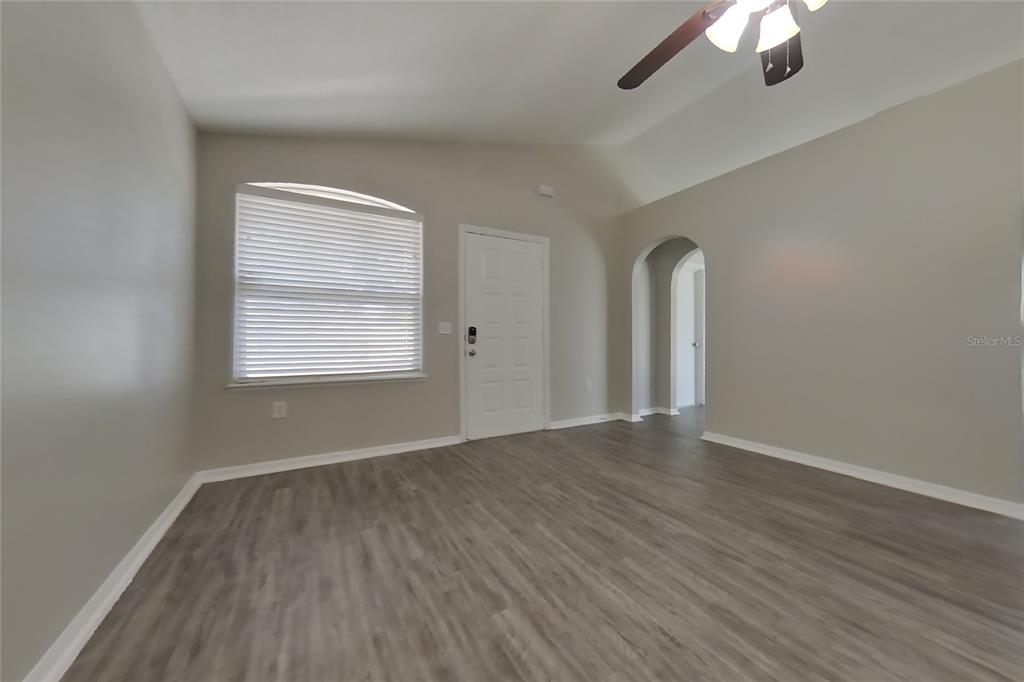 An empty room features light gray walls, wood-look flooring, a ceiling fan, and an arched doorway — 353 COMFORT DRIVE, APOPKA, FL